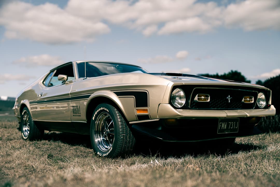 Gold Ford Mustang Mach 1 parked in a field under a cloudy sky