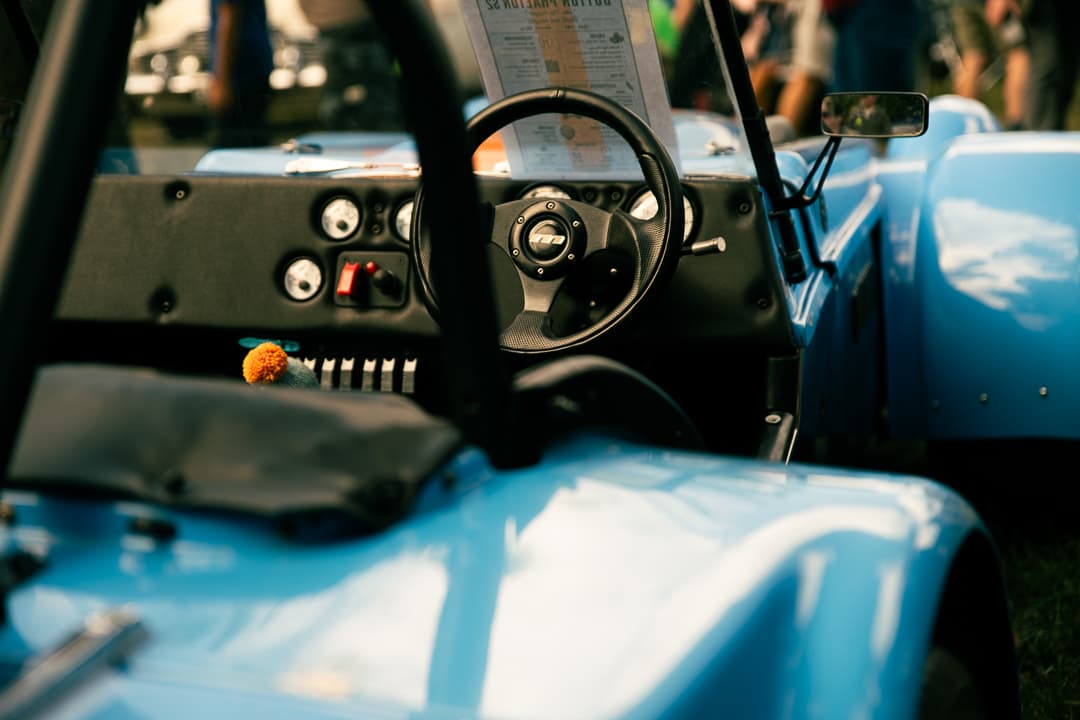 Cockpit of a light blue open-top sports car at a summer car show