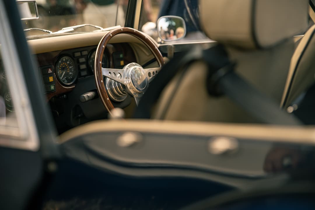 Wood-rimmed steering wheel and cream leather interior of a blue classic sports car
