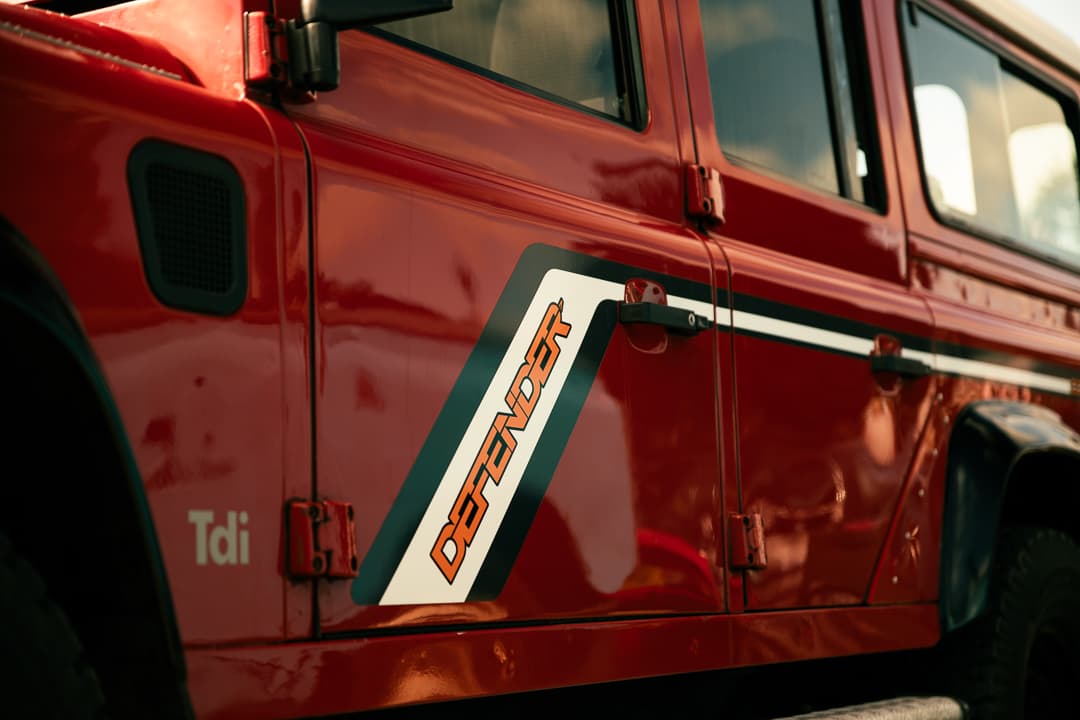 Defender decal and Tdi badge on the side of a red Land Rover Defender
