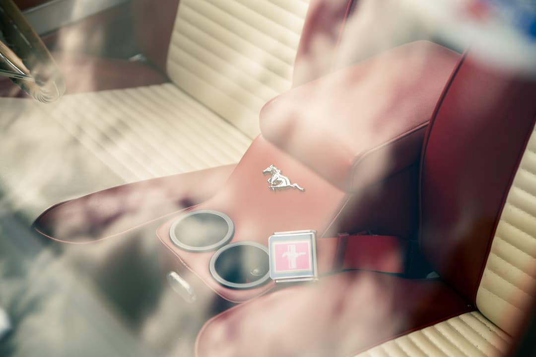 Pony badge and cream leather seats reflected in the window of a classic Ford Mustang