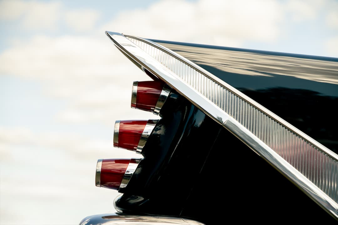 Tail fin and triple rear lights of a 1950s American car against a cloudy sky