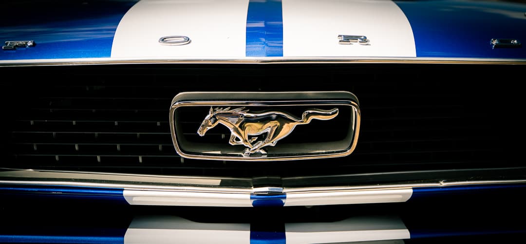 Chrome pony badge in the grille of a blue Ford Mustang with racing stripes