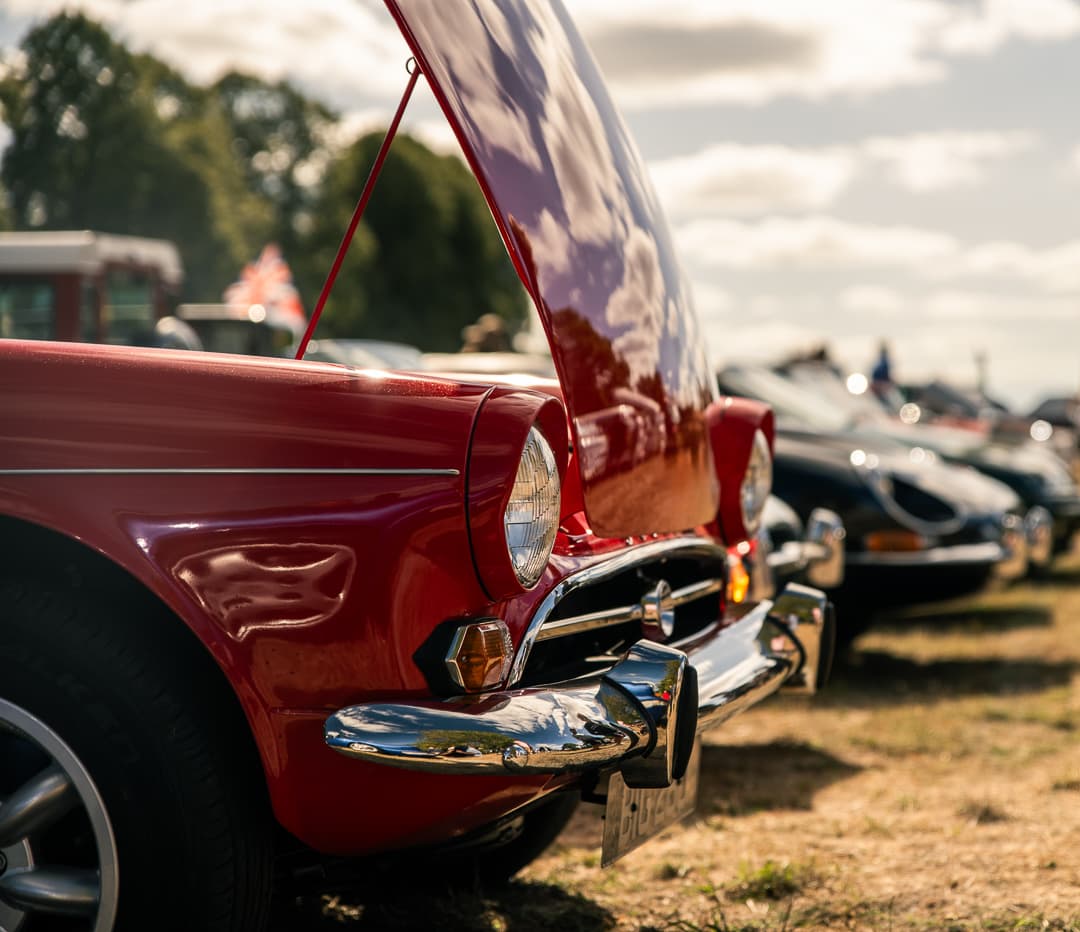 Red classic sports car with its bonnet raised in a field at a car show