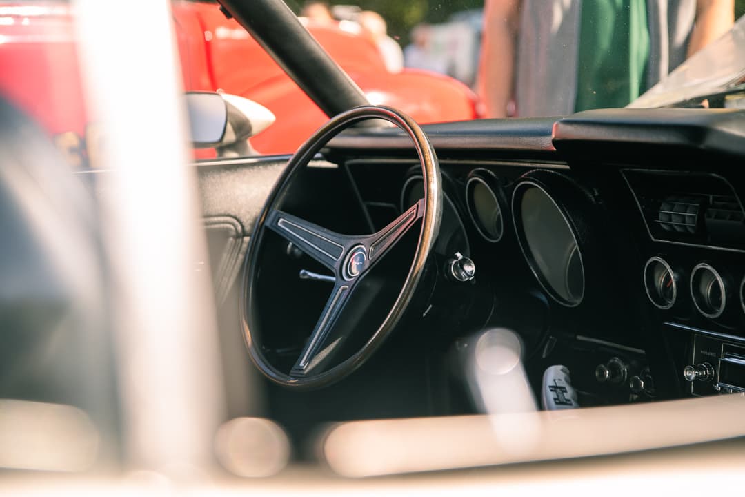 Three-spoke steering wheel and dials seen through the window of a classic sports car