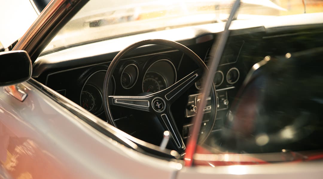 Steering wheel and dashboard dials seen through the windscreen of a silver classic coupe