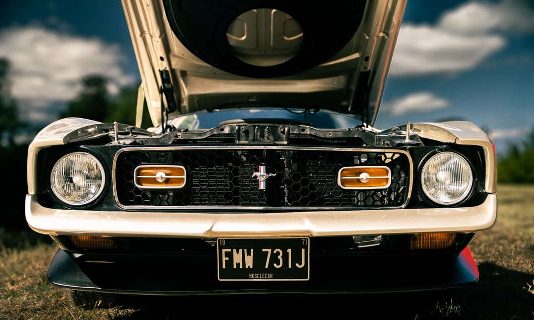 Ford Mustang Mach 1 with its bonnet raised, grille and pony badge lit by low sun