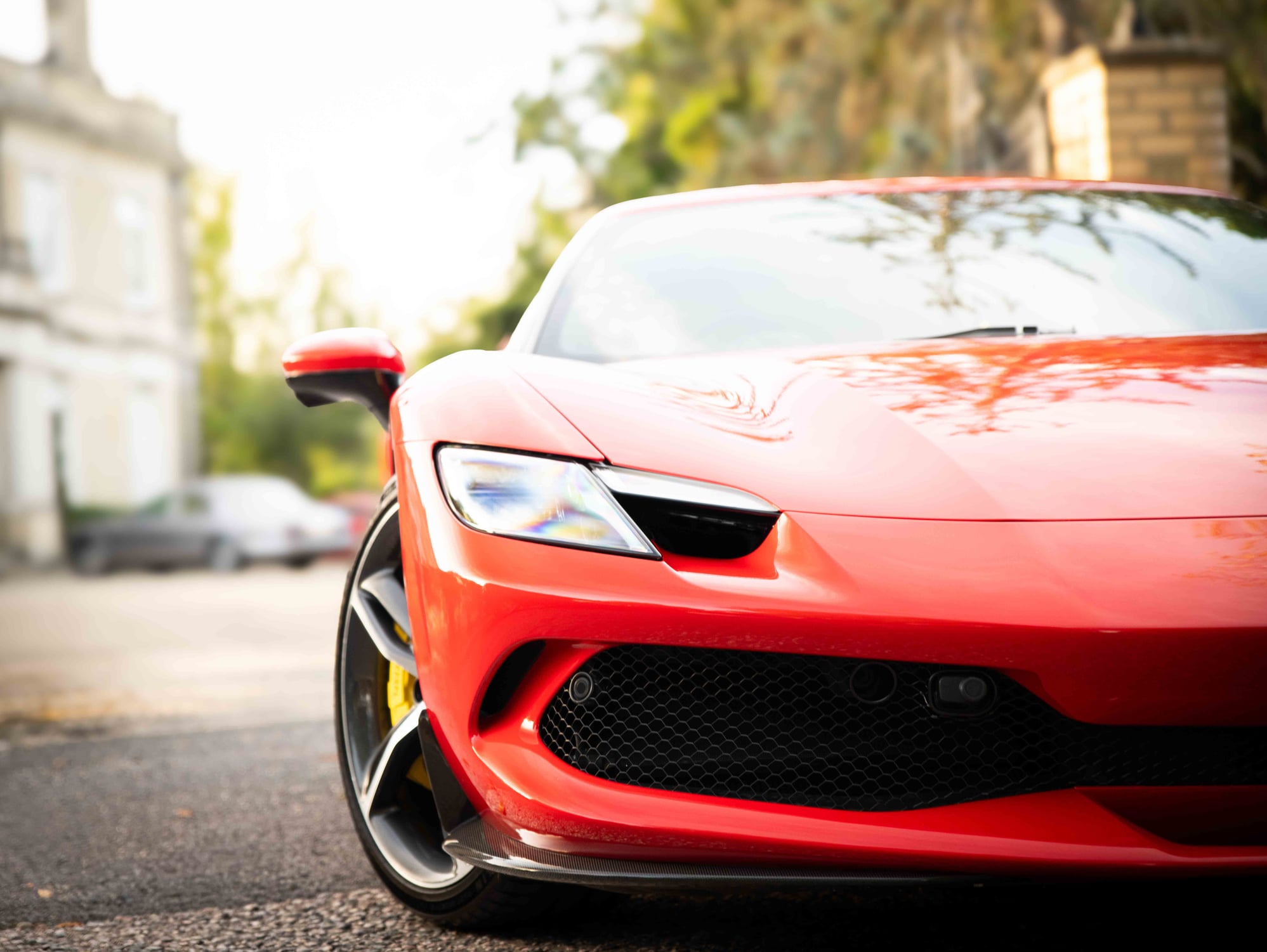 Front corner of a red Ferrari 296 GTB showing the headlight, mirror and honeycomb grille