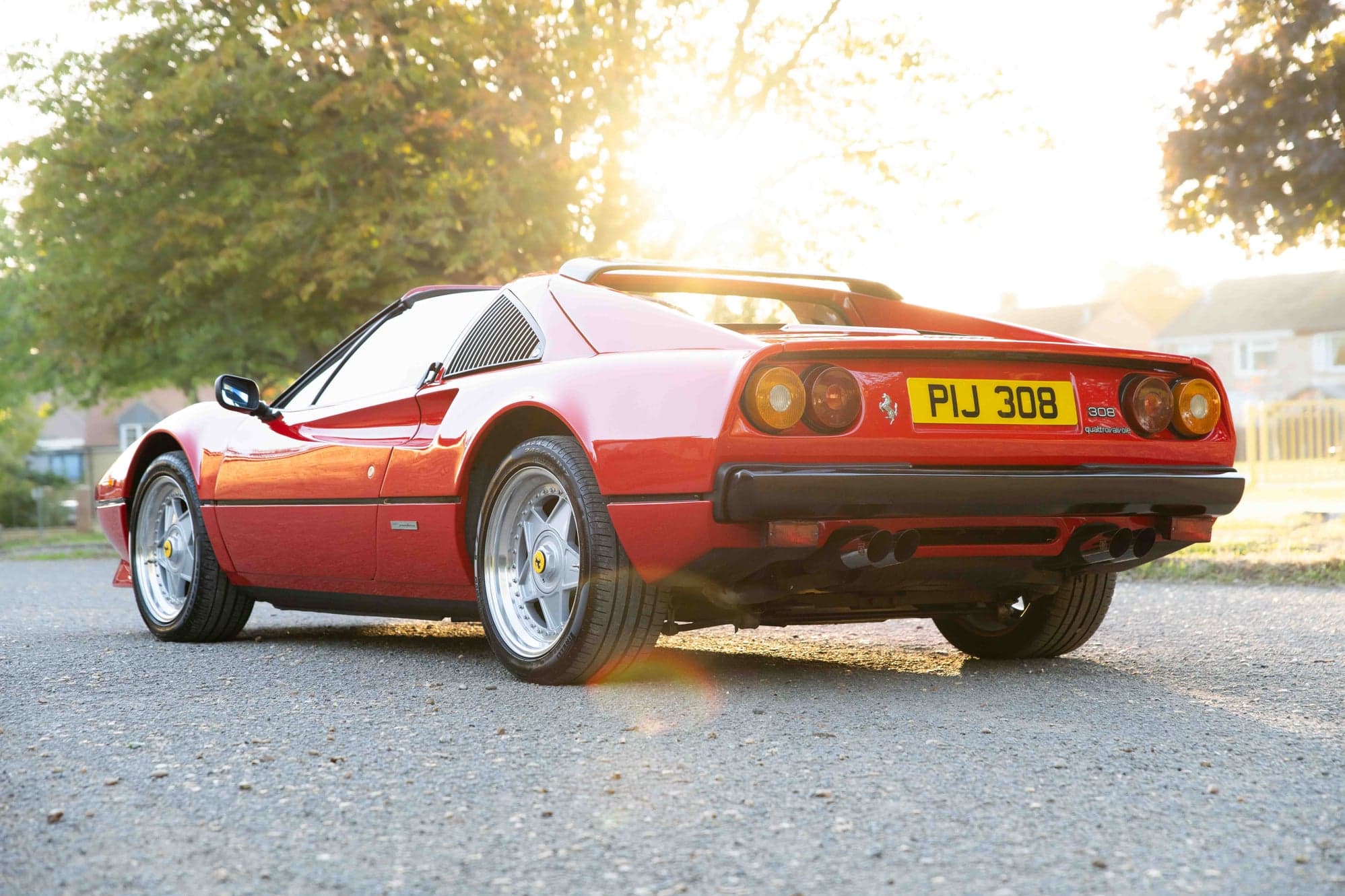 Rear three-quarter view of a red Ferrari 308 GTS backlit by low sun