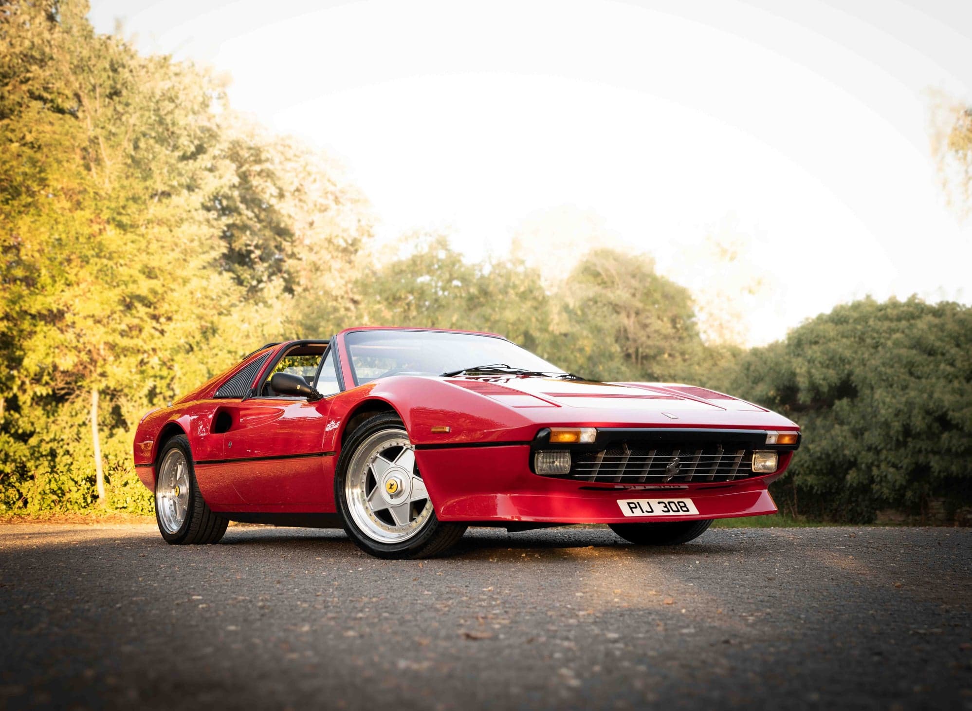 Red Ferrari 308 GTS parked on a lane with autumn trees behind it