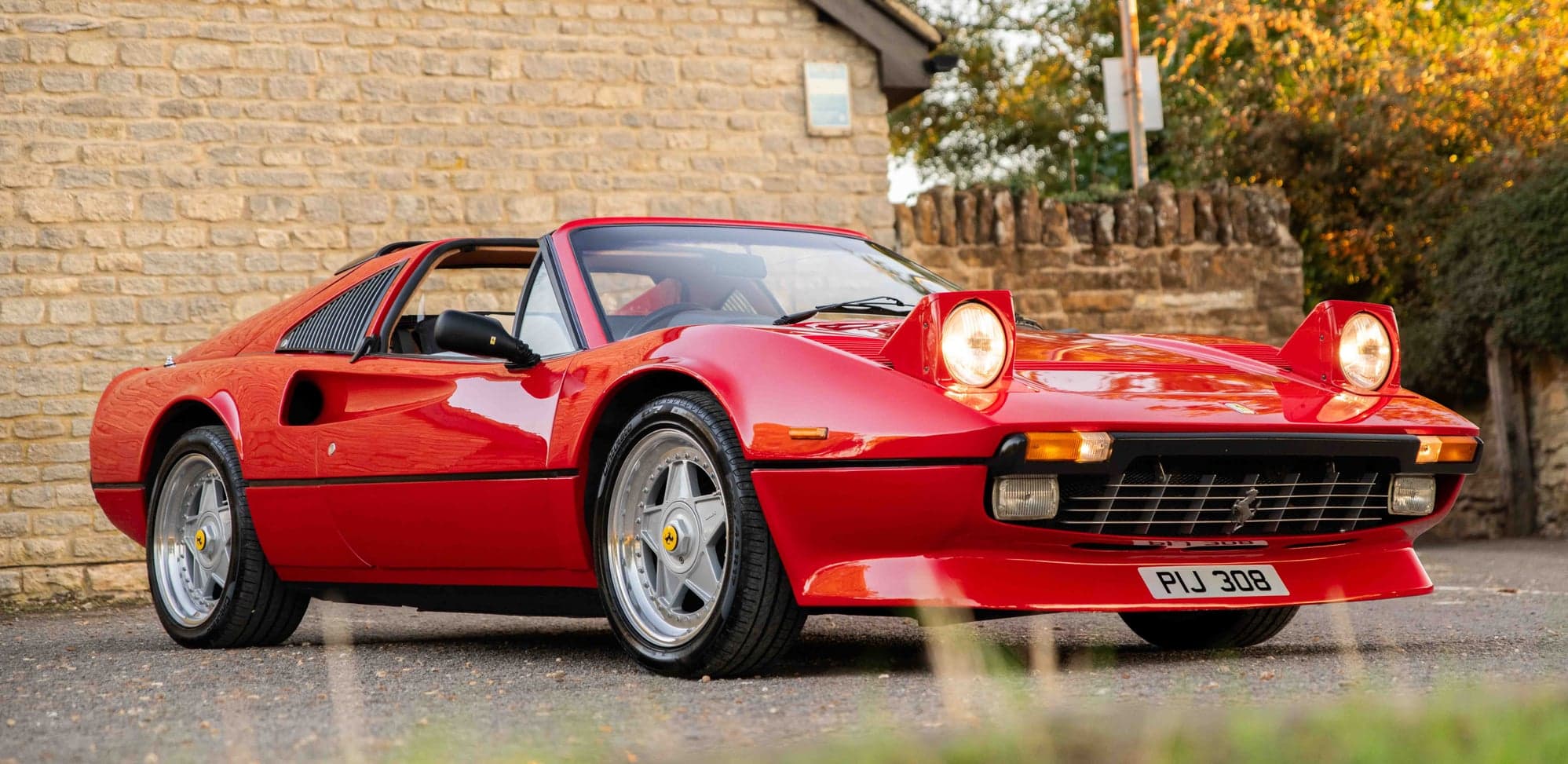 Ferrari 308 GTS with its pop-up headlights raised beside a stone cottage