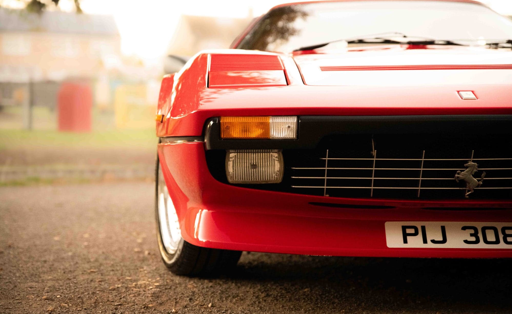 Front corner of a red Ferrari 308 showing the indicator, grille and prancing horse badge
