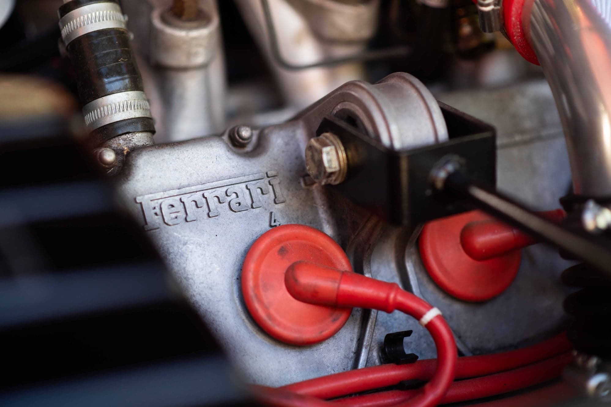 Ferrari cast into the cam cover beside red ignition leads in a 308 engine bay