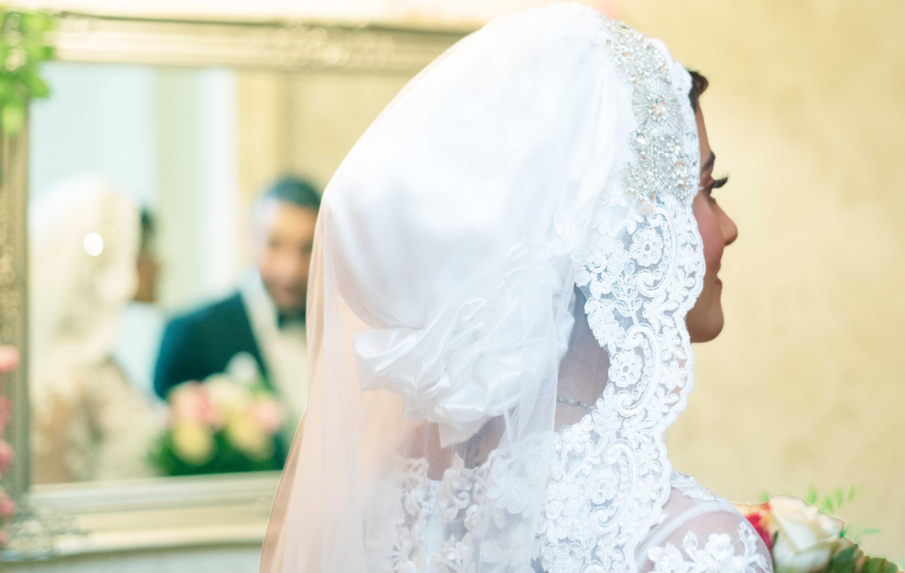 Bride getting ready with groom's reflection in a beautiful mirror