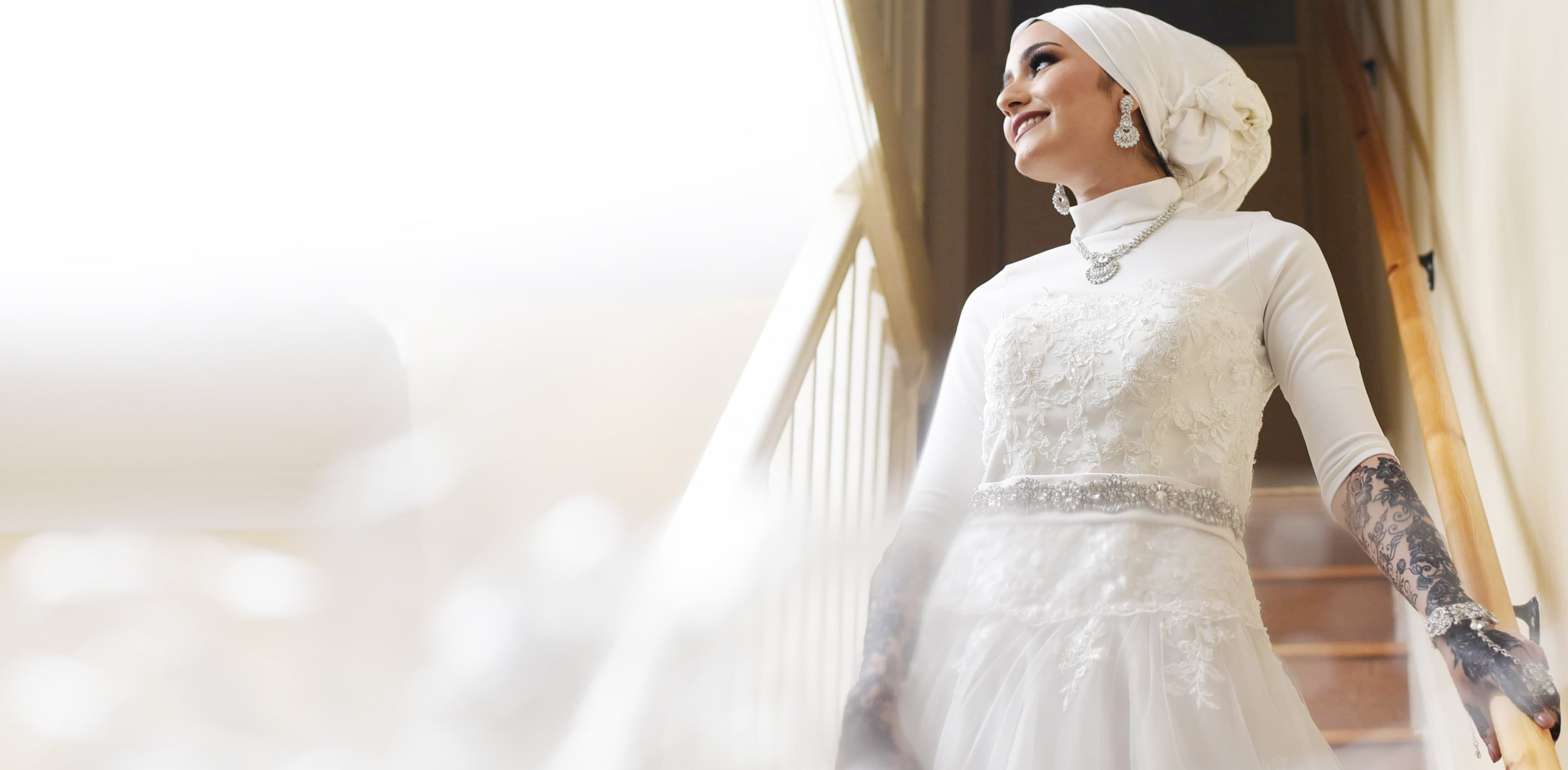 Bride in white dress standing on stairs, gazing down at her loving family