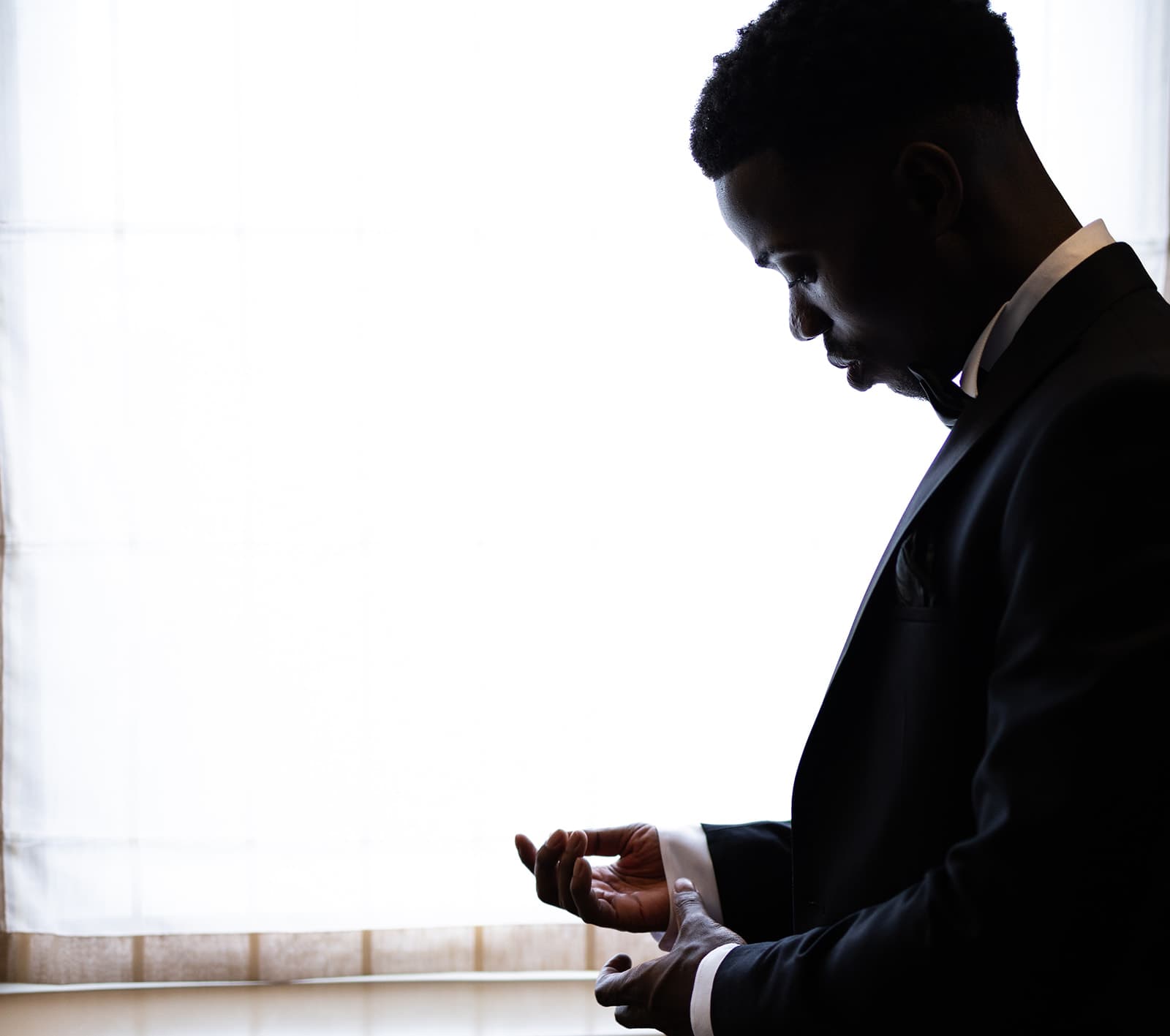 The groom getting ready in the soft light of a hotel window